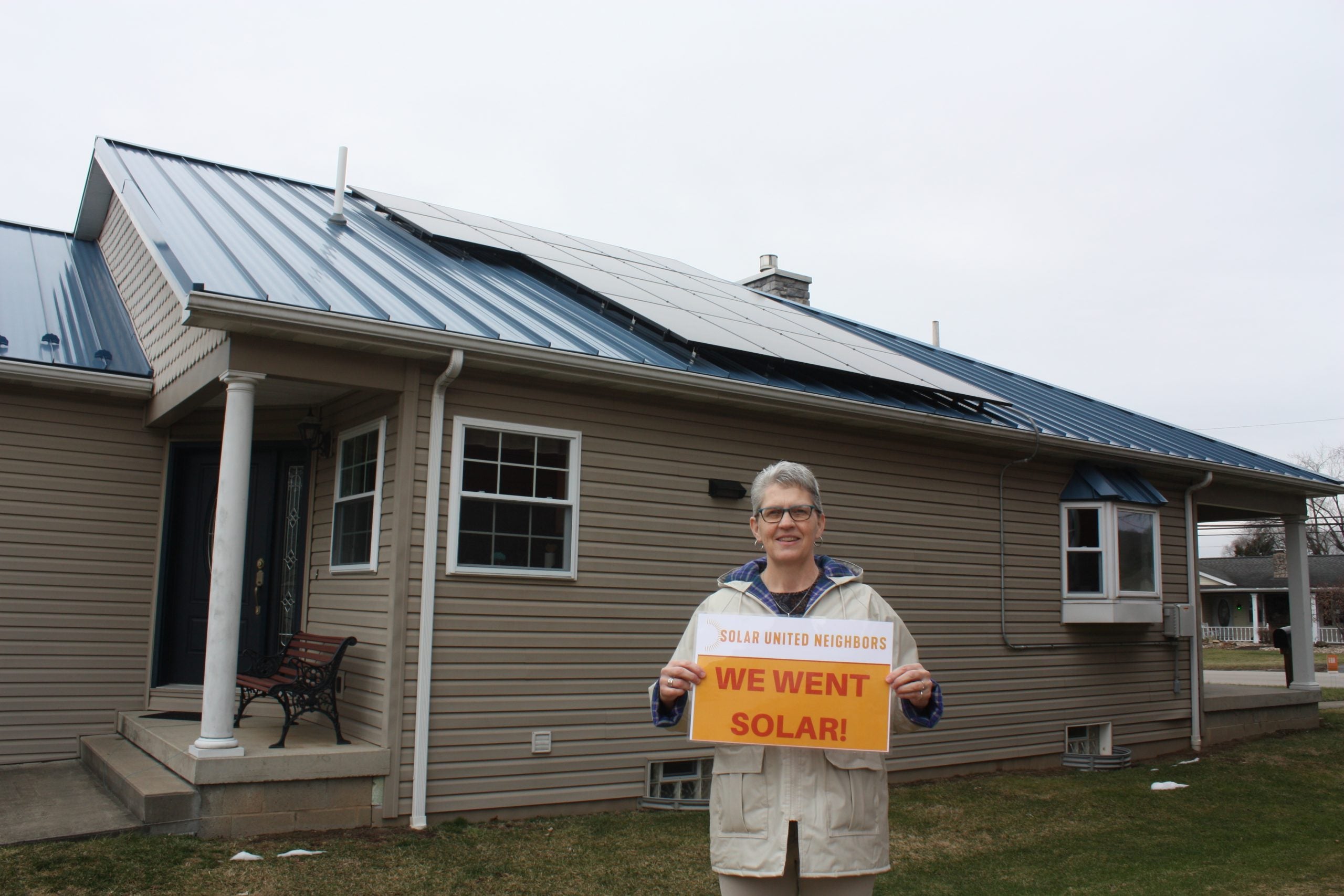 Woman holding a sign that says "we went solar" in front of her home and solar installation
