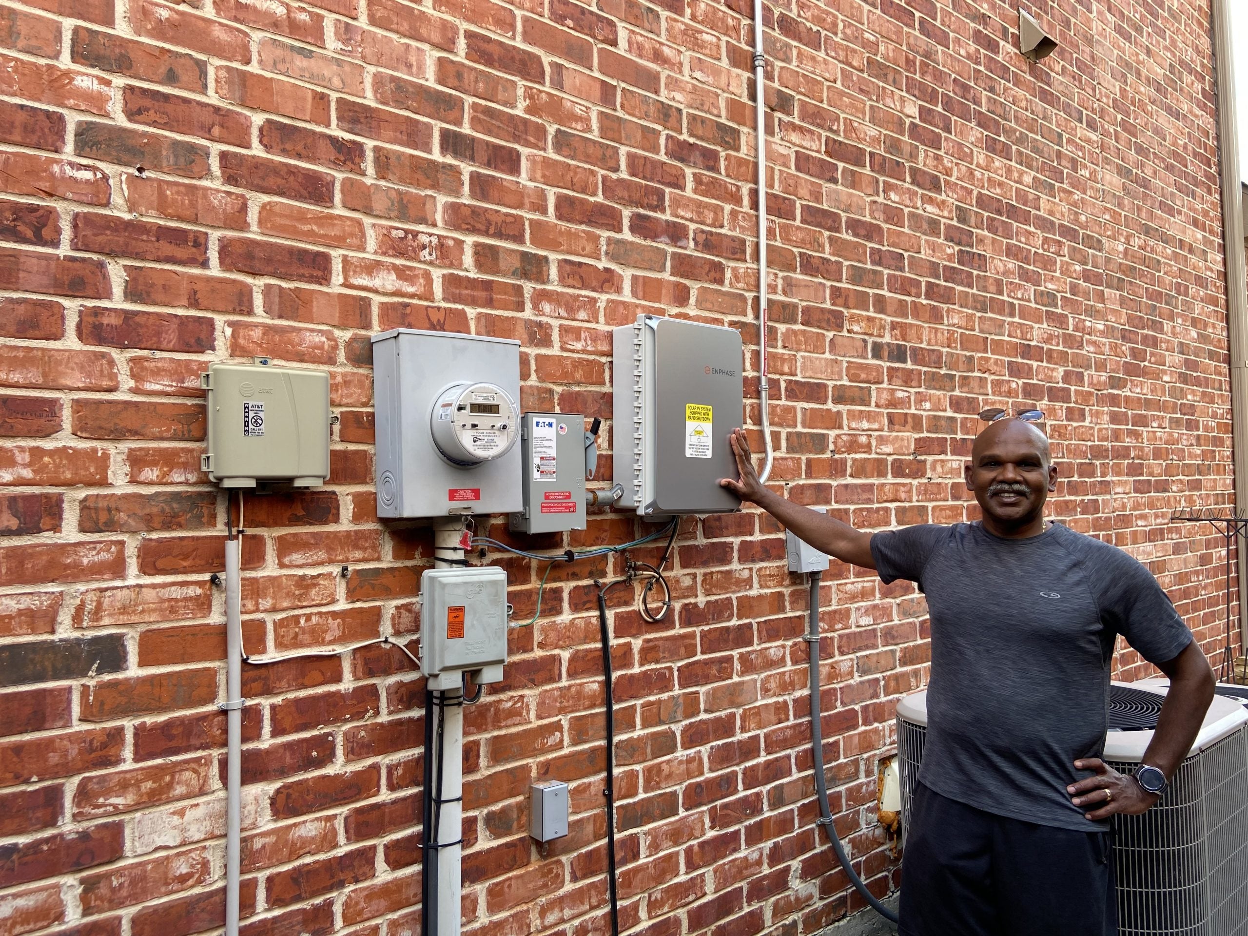 Solar homeowner stands next to his inverter and electric meter