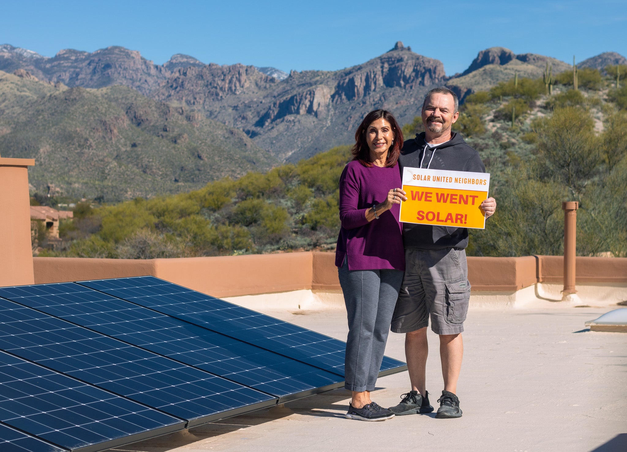 two people on roof with solar panels in front of mountains