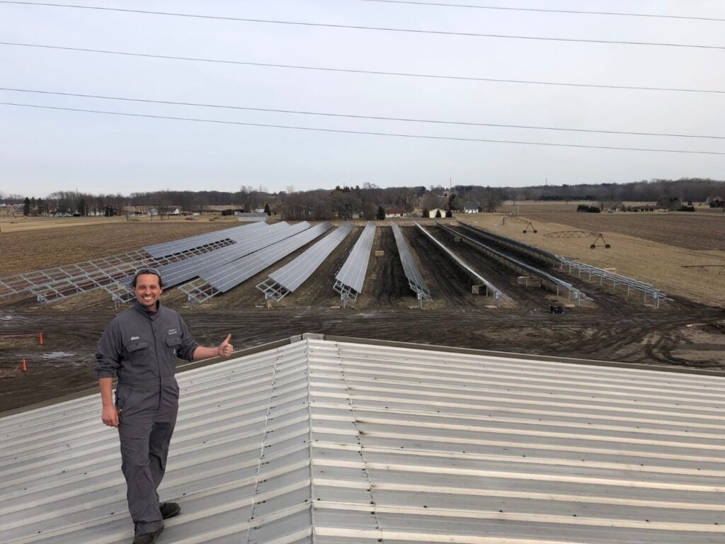 Man standing in front of lines of solar panels in field